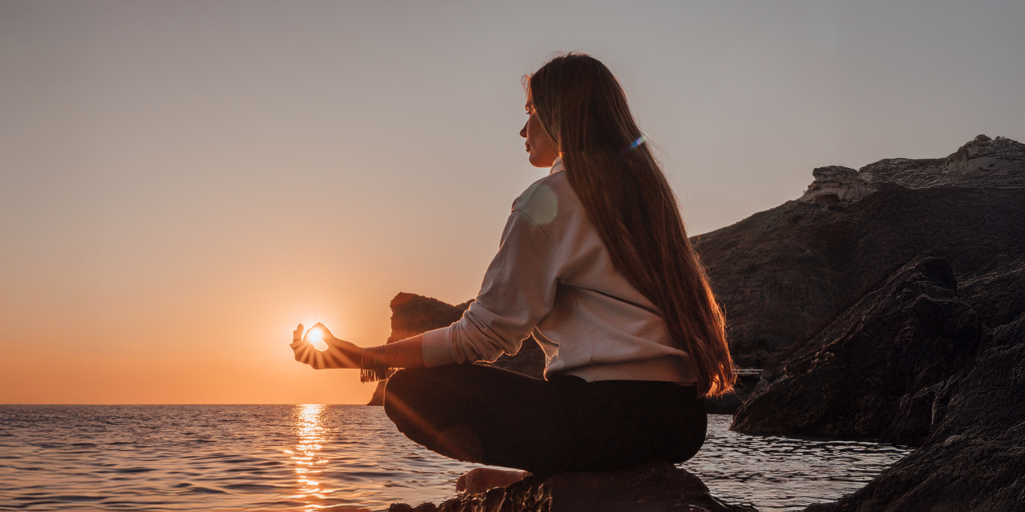 Femme méditant face au coucher du soleil au bord de la mer, symbole de paix intérieure, de clarté mentale et d’éveil spirituel grâce à la méditation.