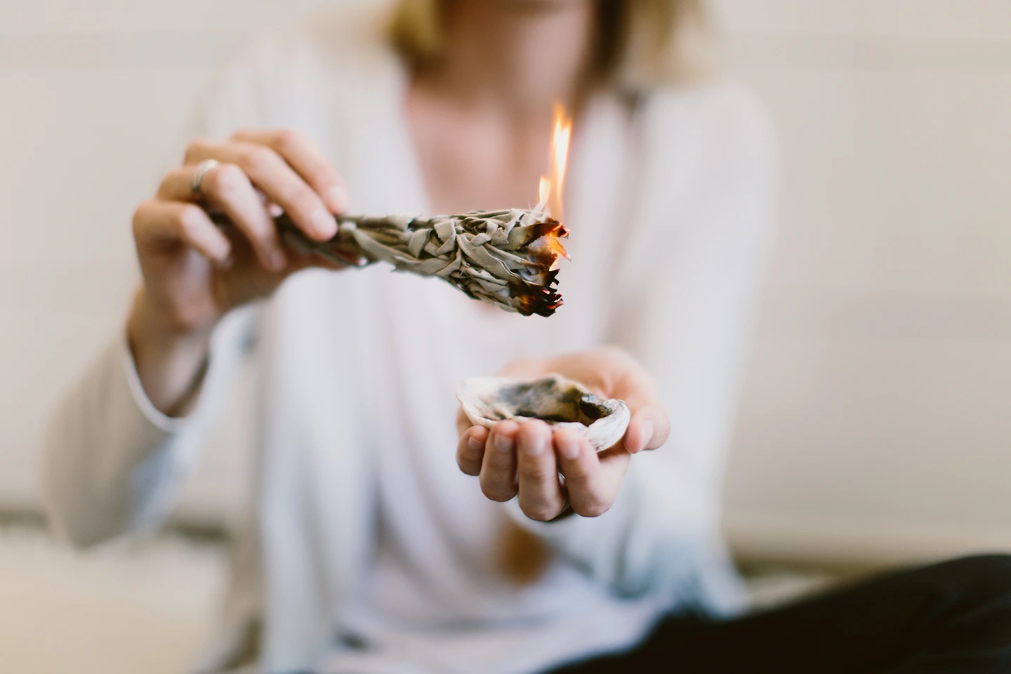 Gros plan sur une personne pratiquant un rituel de purification énergétique avec un bâton de sauge allumé.