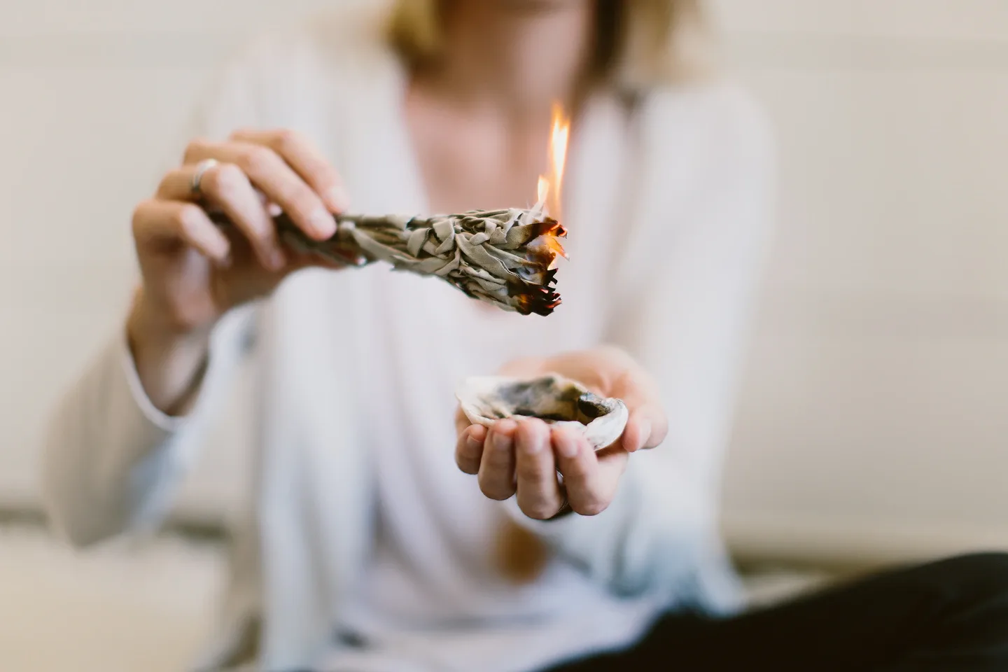 Nahaufnahme einer Person, die ein energetisches Reinigungsritual mit brennendem Salbeibündel durchführt.
