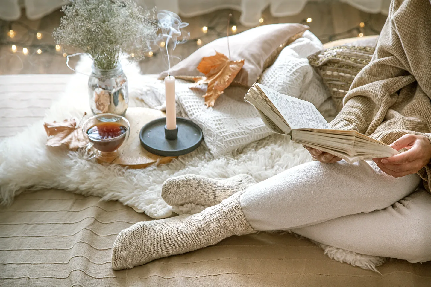 Gemütliche Winteratmosphäre mit einer Frau, die ein Buch liest, einer rauchenden Kerze und einer Tasse Tee – Symbol für spirituelle Winterrituale.