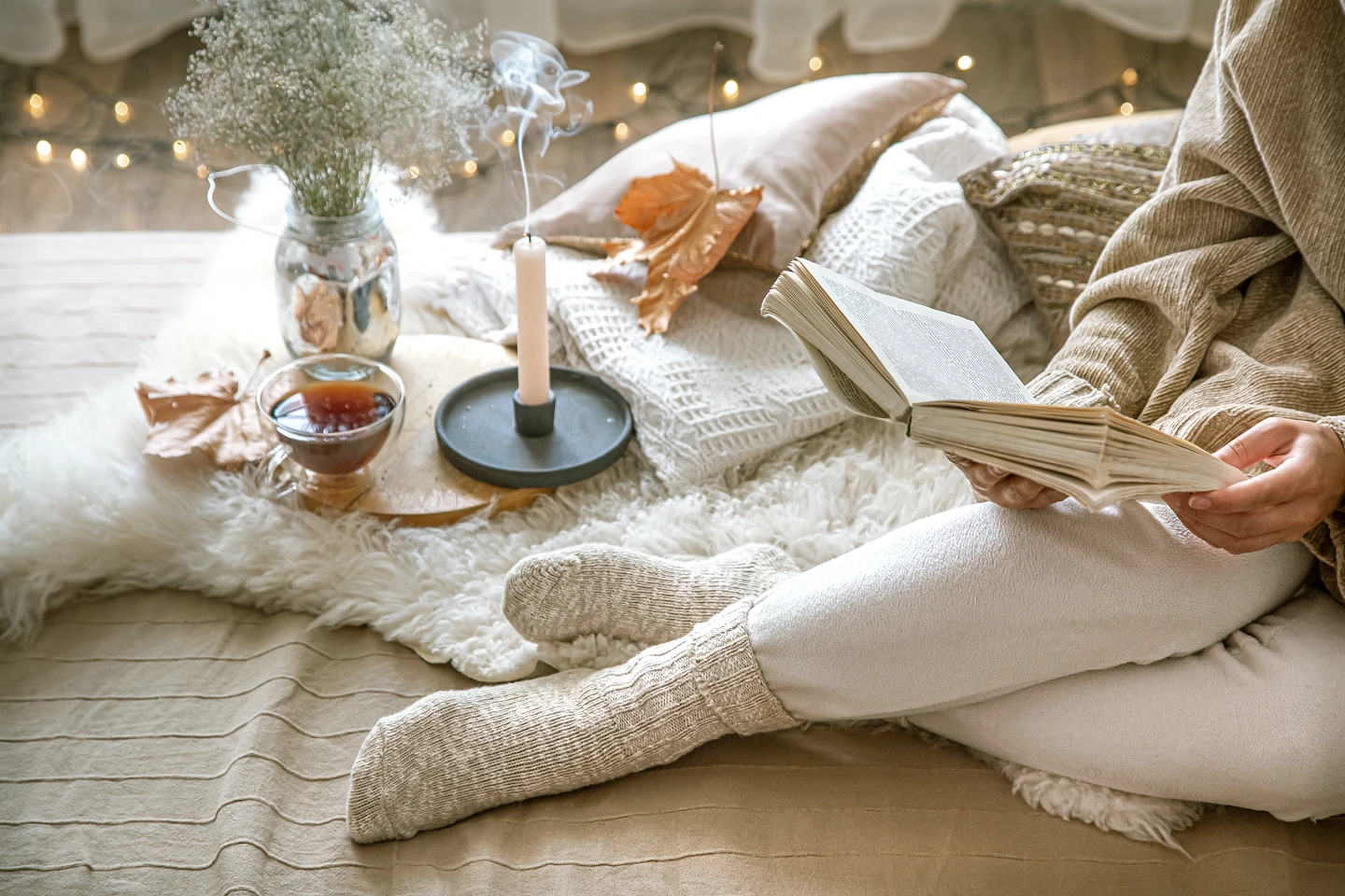 Scène cocooning avec une femme lisant un livre, une bougie fumante et une tasse de thé, illustrant un rituel d’hiver spirituel et apaisant.